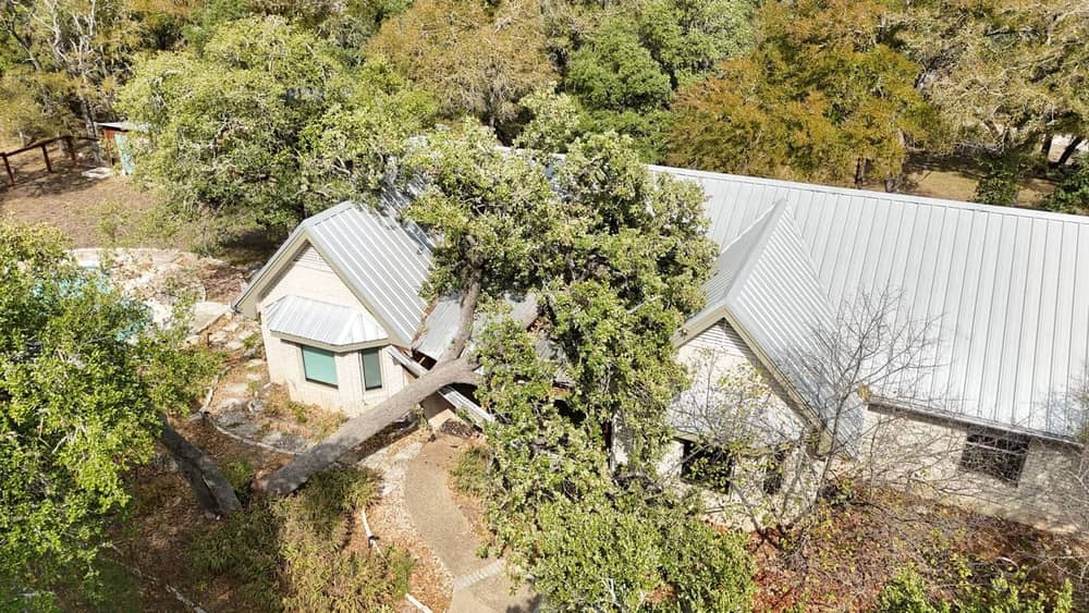 Aerial view of a fallen oak tree crushing a metal roof valley after a storm