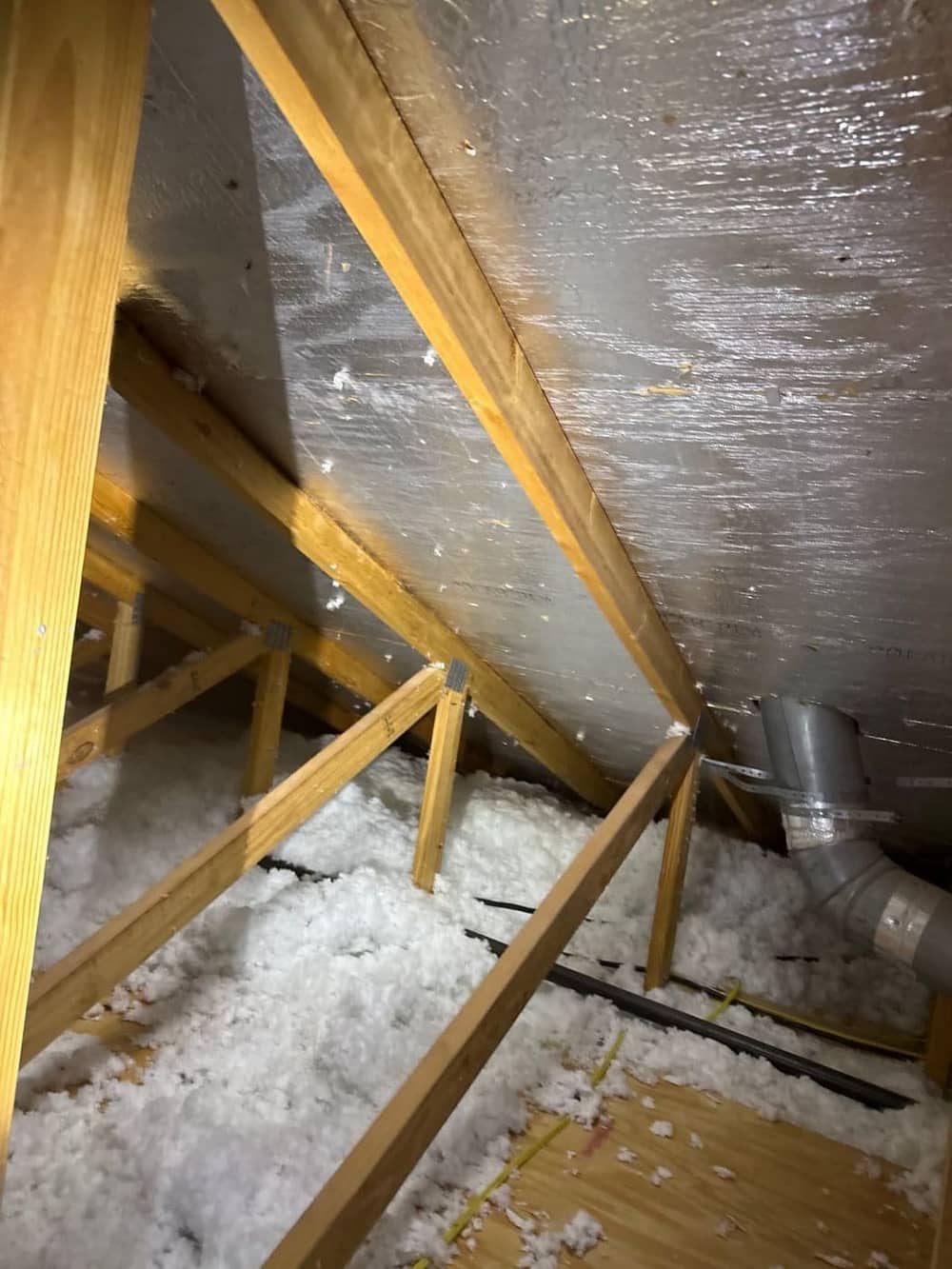 Inside an attic: rafters, radiant-barrier decking and blown insulation, with a vent duct running up to the roof