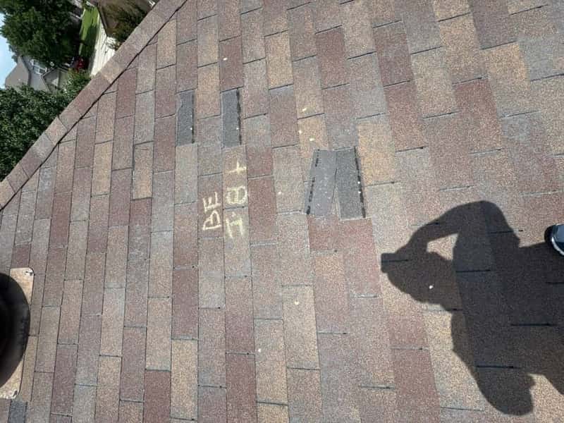 Shingle roof marked with chalk hail-inspection lettering across one slope