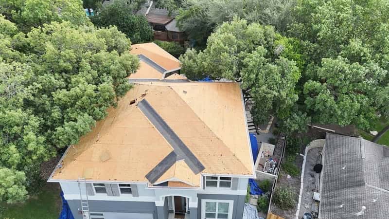 Drone view of a large tree-shaded home mid re-roof with fresh plywood decking installed